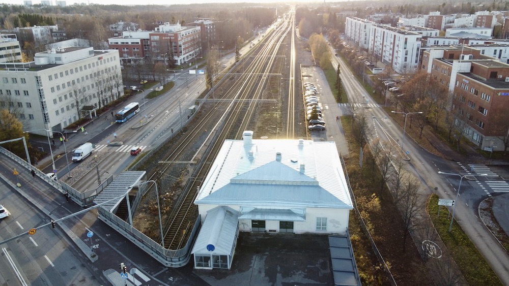 Malmin vanhan asema ja sen uusi katto 30-40 metrin korkeudelta, edestä dronella kuvattuna. Rautatie kulkee suoraan horisonttiin, jossa paistaa aurinko.